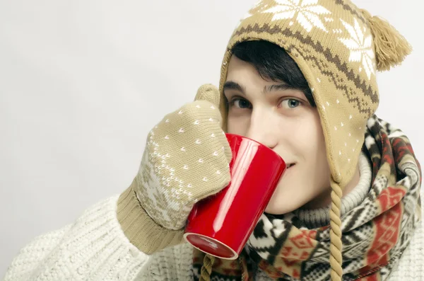 Портрет красивые мужчины носить свитер, перчатки, шарф и шляпу, одетый в зимнюю стужу и выпивать чашку горячего чая
