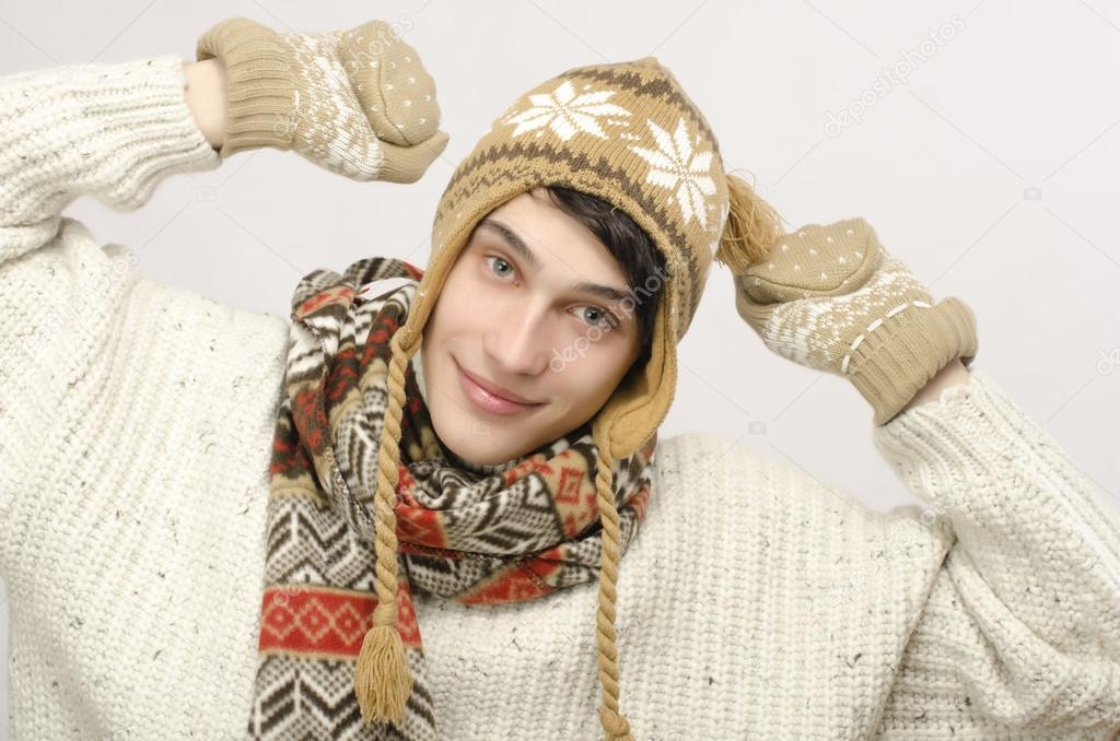 Portrait of a beautiful man wearing sweater, gloves, scarf and a hat, dressed for winter cold, smilling