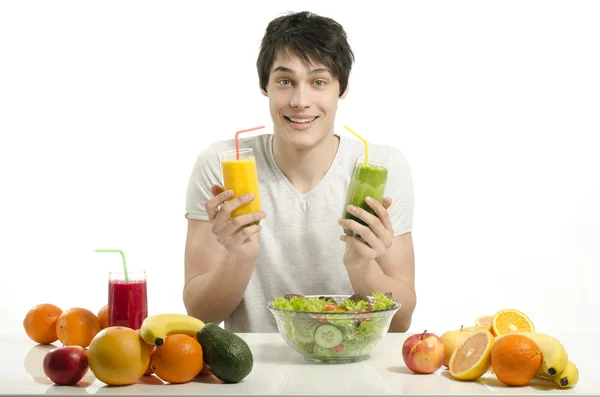 Hombre feliz eligiendo entre jugo de naranja y batido verde. Joven alegre comiendo ensalada saludable y frutas. Aislado sobre blanco . —  Fotos de Stock
