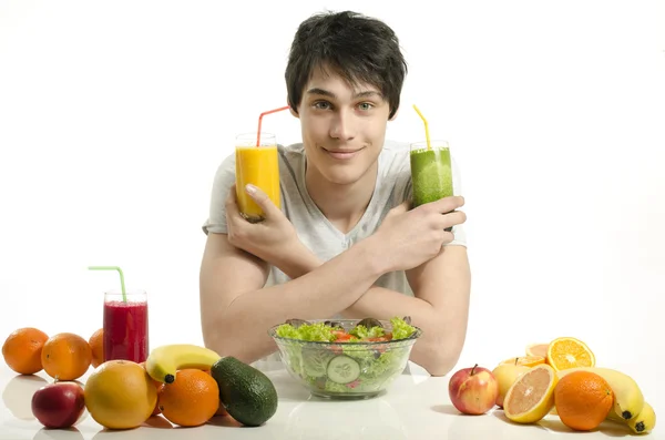 Hombre feliz eligiendo entre jugo de naranja y batido verde. Joven alegre comiendo ensalada saludable y frutas. Aislado sobre blanco . — Foto de Stock