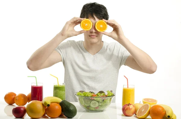 Happy man holding in front of his eyes oranges. Cheerful young man eating healthy salad, fruits , orange juice and green smoothie. — Stock Photo, Image