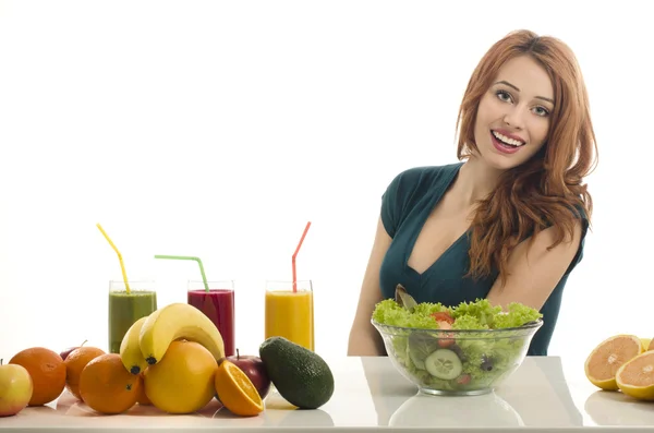 Mujer feliz teniendo una mesa llena de comida orgánica, jugos y batidos. Joven alegre comiendo ensalada saludable y frutas. Aislado sobre blanco . —  Fotos de Stock