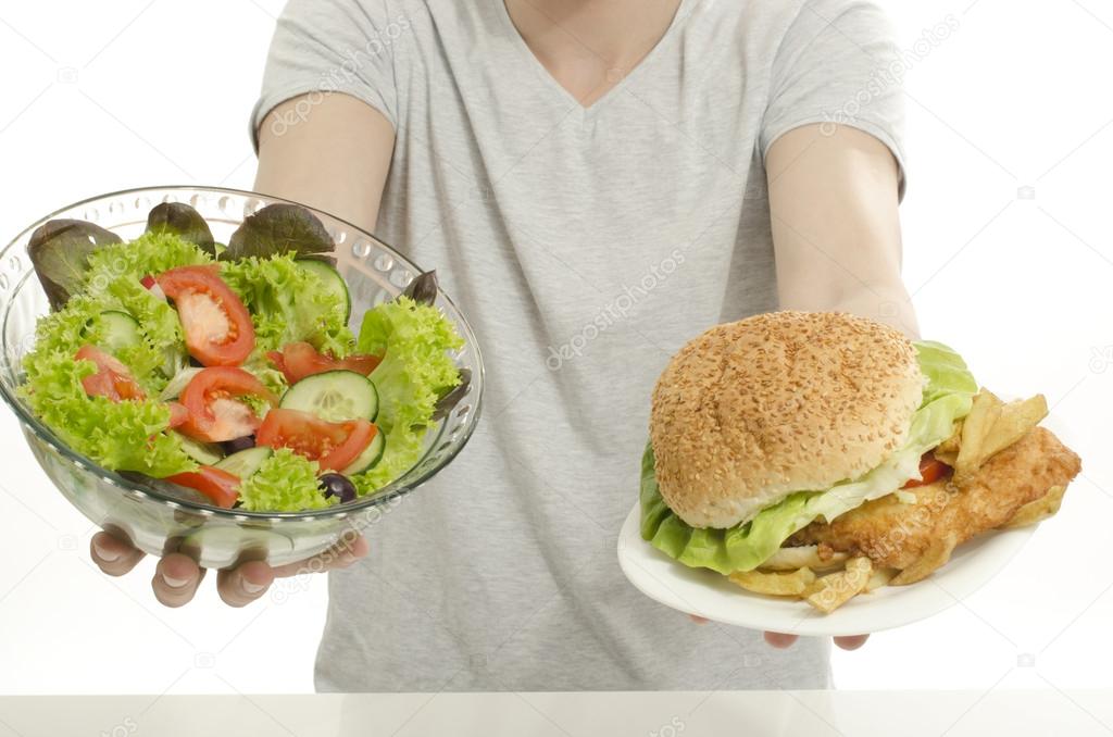 Man hands offering you a salad and a hamburger. Unrecognizable person holding in front a bowl of salad and a big burger. Choosing between good healthy food and bad unhealthy food.