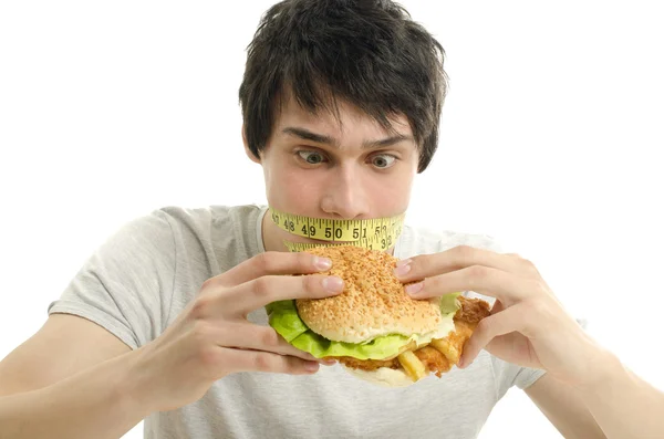 Hombre con un centímetro en la boca incapaz de comer una hamburguesa grande, hombre joven a dieta y tener un tiempo difícil con la comida rápida —  Fotos de Stock