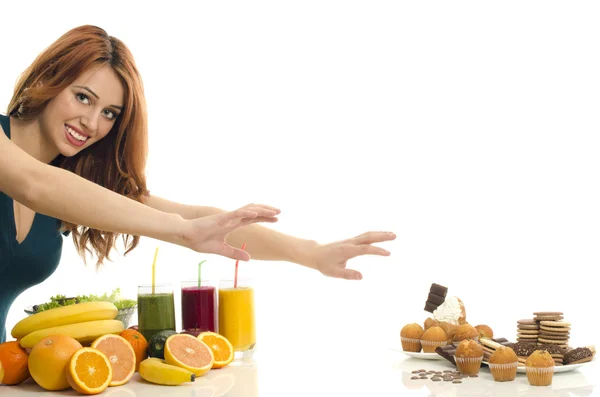 Woman choosing between fruits, smoothie and organic healthy food against sweets, sugar, lots of candies, unhealthy food — Stock Photo, Image