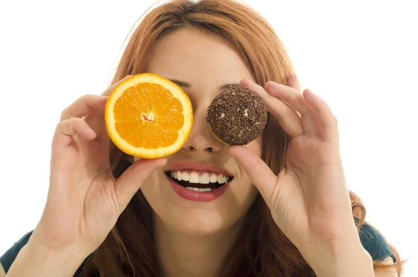 Frau hält eine Orange und eine Süßigkeit vor ihren Augen und wählt zwischen gesundem und ungesundem Essen — Stockfoto