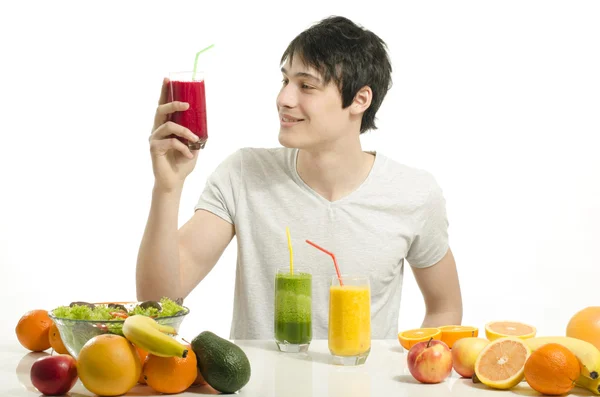 Glücklicher Mann mit einem Tisch voller Biolebensmittel, Säften und Smoothie. fröhlicher junger Mann, der gesunden Salat und Obst isst. isoliert auf weiß — Stockfoto