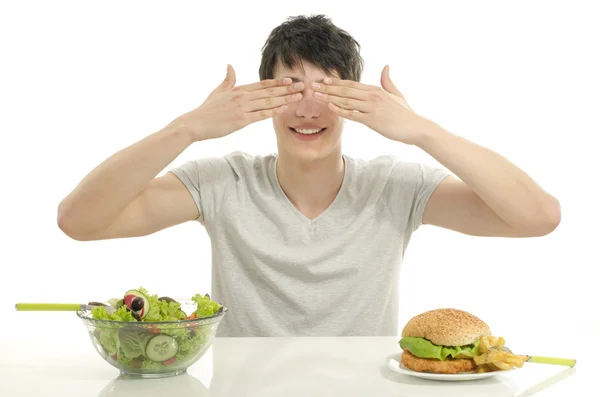 Um homem a oferecer-te uma salada e um hambúrguer. Jovem segurando na frente uma tigela de salada e um grande hambúrguer. Escolhendo entre boa comida saudável e má comida não saudável — Fotografia de Stock