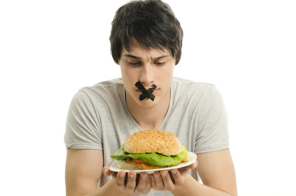 Man with a black tape on his mounth unable to eat a big hamburger, young man dieting and having a hard time with fast food — Stock Photo, Image