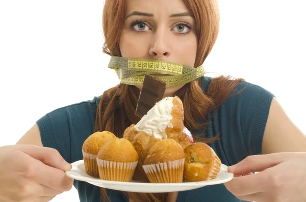 Mujer con un centímetro en la boca incapaz de comer todos los dulces y azúcar, un montón de galletas en un plato —  Fotos de Stock