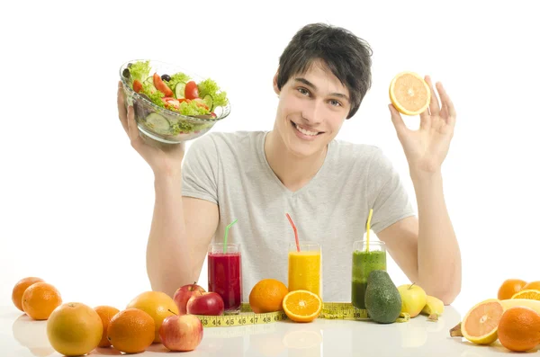 Szczęśliwy człowiek o stół pełne żywności ekologicznej, soki i koktajl. wesoły młody człowiek jedzenie zdrowe sałatki i owoce. na białym tle — Zdjęcie stockowe