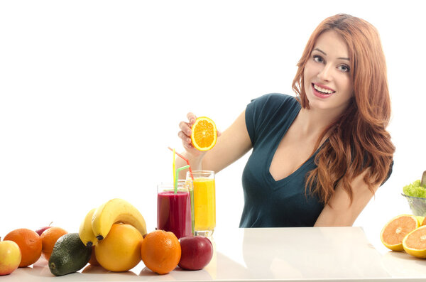 Woman squeezing and orange and preparing an organic juice. Happy woman having a table full of organic food,juices and smoothie. Cheerful young woman eating healthy salad and fruits. Isolated on white.