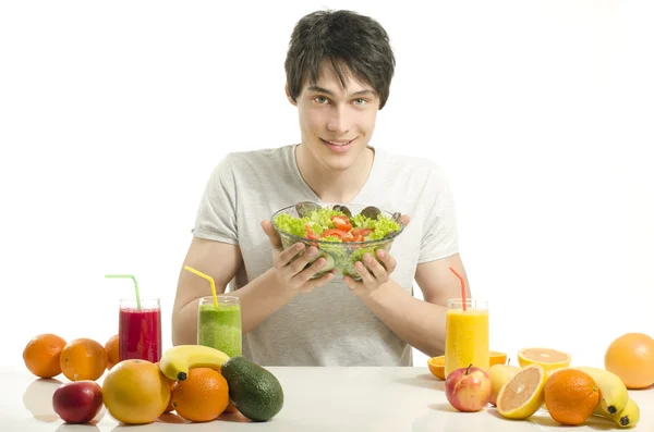 Uomo felice avere un tavolo pieno di cibo biologico, succhi di frutta e frullato. Giovane allegro mangiare insalata sana e frutta. Isolato su bianco . — Foto Stock