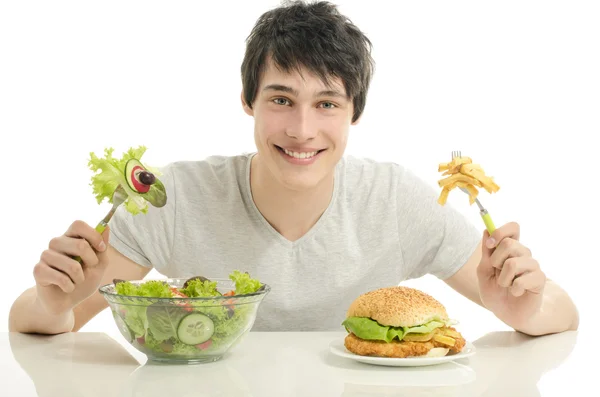Jovem segurando na frente uma tigela de salada e um grande hambúrguer. Escolhendo entre boa comida saudável e má comida não saudável — Fotografia de Stock