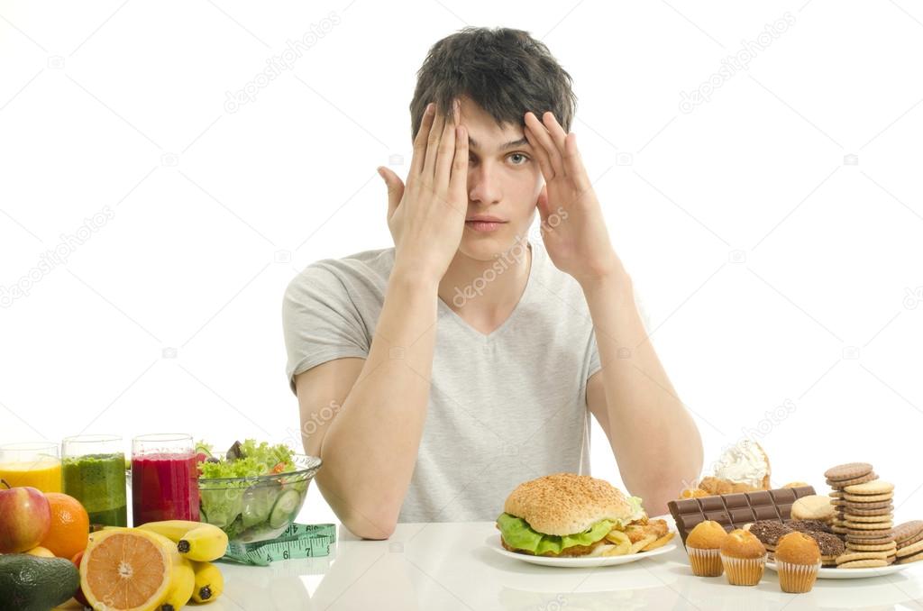 Man choosing between fruits, smoothie and organic healthy food against sweets, sugar, lots of candies and a big hamburger, unhealthy food