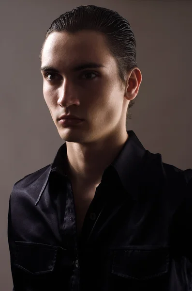 Portret van een mooie jonge man gekleed in een zwarte shirt. gezicht van een man in schaduwen — Stockfoto