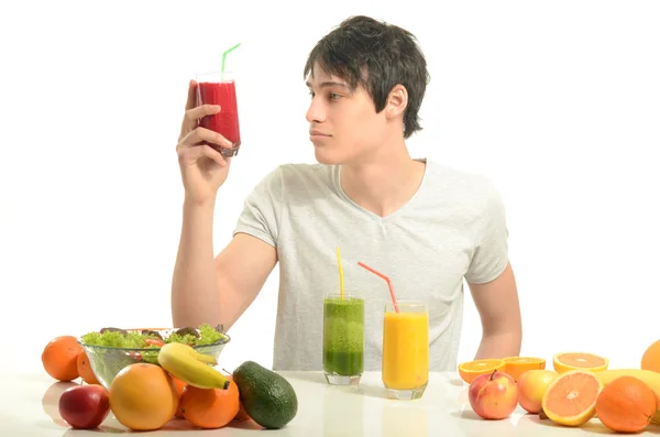 幸せな男は、有機食品、ジュース、スムージーの完全なテーブルを持っています。陽気な若い男が健康的なサラダや果物を食べるします。白で隔離されます。. — ストック写真