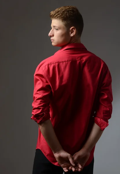 Hermoso joven con una camisa roja posando con la espalda y mirando a la luz — Foto de Stock