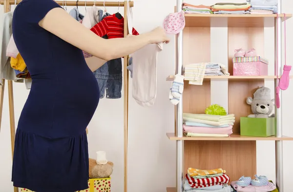 Pregnant woman shopping for clothes for her newborn baby. Dressing closet with clothes arranged on hangers.Colorful wardrobe of newborn,kids, babies full of all clothes, shoes,accessories and toys — Stock Photo, Image