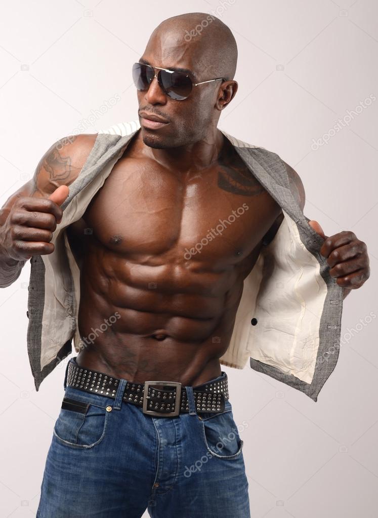 Bodybuilder with sunglasses undressing and showing his muscles. Strong man with perfect abs, shoulders,biceps, triceps and chest. Isolated on white background