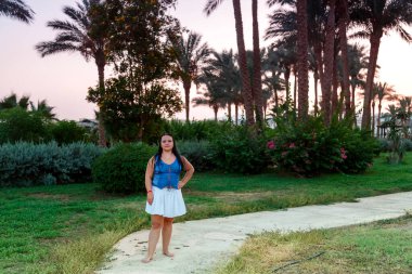 Beyaz etekli Yahudi bir kadın gün batımında palmiye ağaçları ve deniz kenarında bir patika boyunca yürür. Yatay fotoğraf