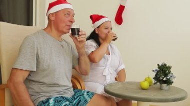 Noel Baba şapkalı karı koca Noel 'i balkonda kutluyor, masada bir kokteyl içiyor, küçük bir Noel ağacı.