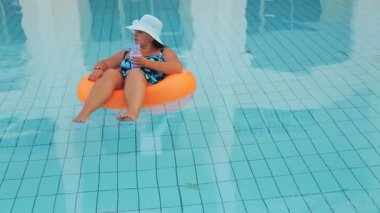 Güneş şapkalı neşeli kadın ve yüzme havuzunda mayo yavaşça yüzer ve dinlenir..