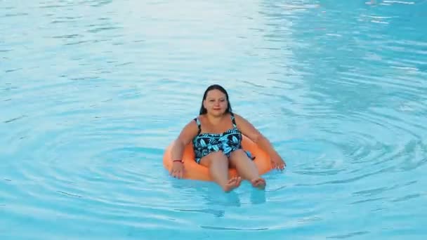 Židovka v klobouku v plavkách v bazénu v plaveckém kruhu pomalu plave — Stock video