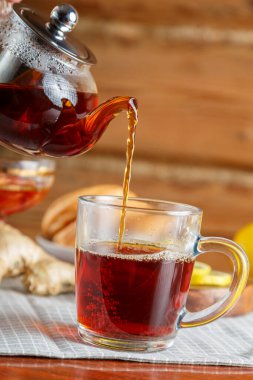 Arkaplandaki limonlu zencefilli çaydanlıktan koyu doymuş çay bir fincana dökülür. Dikey fotoğraf