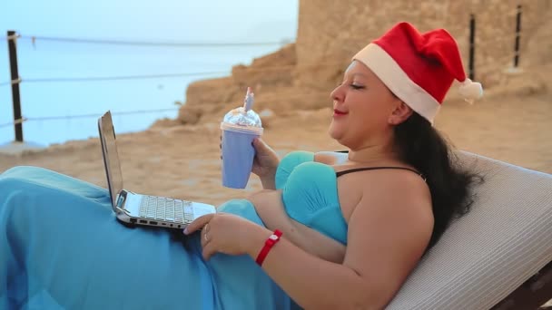 Μια Γυναίκα Στην Παραλία Μια Ξαπλώστρα Καπέλο Αγίου Βασίλη Πίνει — Αρχείο Βίντεο