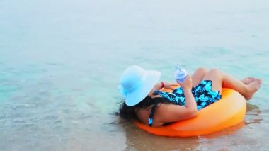 Noel Baba şapkası ve güneş gözlüklü esmer bir kadın Noel tatilinde elinde bir Noel ağacıyla denizde daireler çizerek yüzer. Genel plan