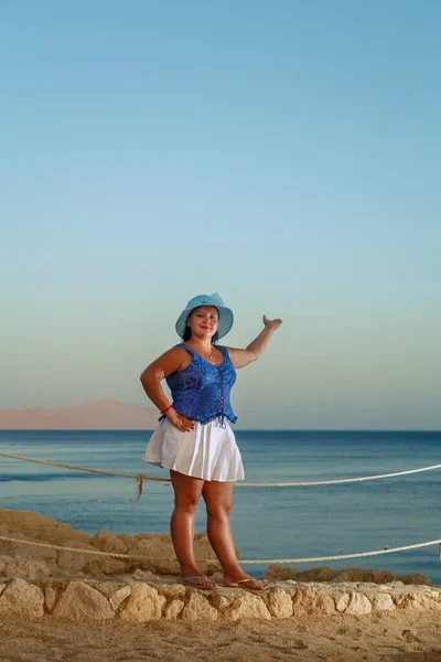Una mujer joven con una falda blanca y un sombrero de sol en la orilla del mar se ve desde una altura. — Foto de Stock