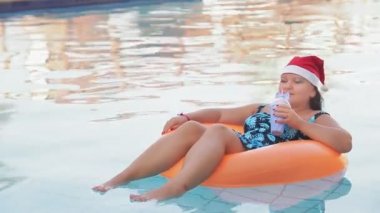 Havuzda yüzme çemberinde Noel Baba şapkalı bir kadın kutlama için kokteyl içiyor. Ortam planı