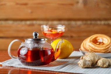 Masanın üzerinde limon, zencefil, reçel ve çöreğin yanındaki peçetenin üzerinde sıcak bir çaydanlık..