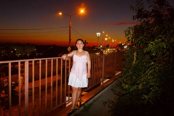 Una joven camina al atardecer por una calle iluminada de la ciudad. —  Fotos de Stock