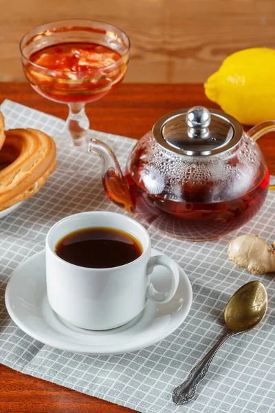 En tekanna och en kopp starkt aromatiskt te på bordet bredvid ingefära och citron ldem och munkar. — Stockfoto