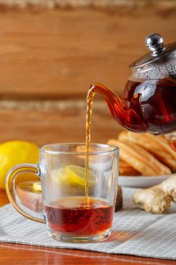 Koyu doymuş çay, limon ve zencefilin yanındaki cam çaydanlıktan bir fincana dökülür..