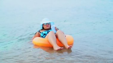 Mavi şapkalı ve güneş gözlüklü esmer bir kadın denizde daireler çiziyor ve uzaklığa bakıyor.