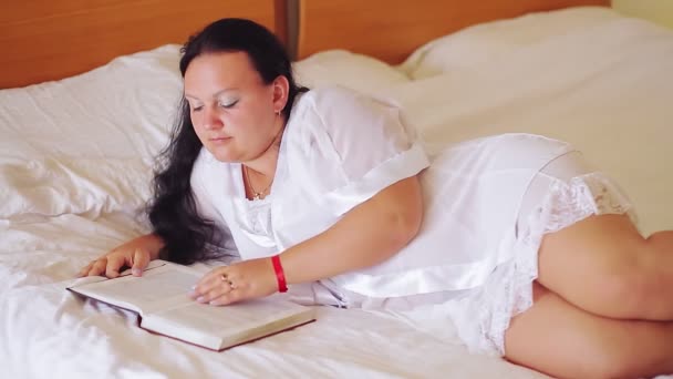 広いベッドの上に白い衣を着た女性が本を読んでいる — ストック動画