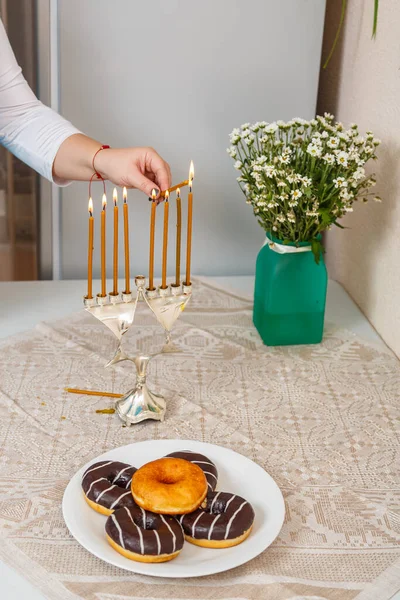 餐厅厨房里的一位犹太妇女的手点燃了靠近甜甜圈桌上的蜡烛和一个花瓶. — 图库照片
