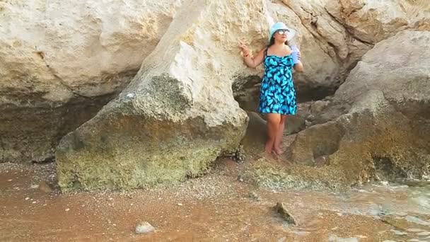 Женщина в синей шляпе и сарафане гуляет по побережью Красного моря в солнечный день среди зеленых насаждений — стоковое видео