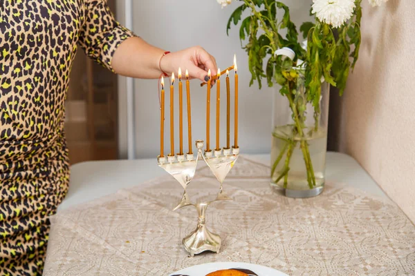 一位犹太妇女的手在靠近节日花圈的桌子上的一盏光明灯和一个花瓶里点燃着蜡烛. — 图库照片