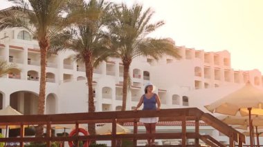 Köprüde mavi şapkalı esmer bir Yahudi kadın otelin arka planındaki palmiye ağaçlarına hayran.