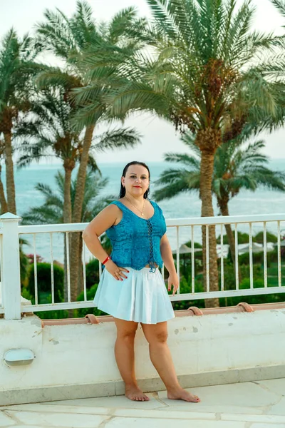 Una mujer judía con una falda blanca se levanta en la barandilla contra el telón de fondo de las palmeras y el mar. — Foto de Stock