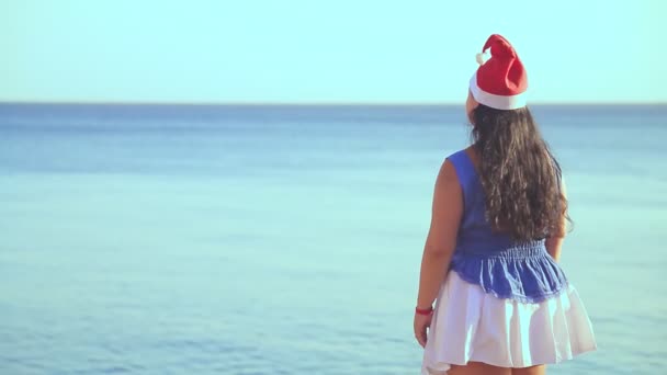 Brunette nainen Santa hattu seisoo kiviä meren ihaillen luontoa — kuvapankkivideo