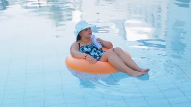 Güneş şapkalı neşeli kadın ve yüzme havuzunda mayo giyen yüzen kadın meşrubat içer ve dinlenir..