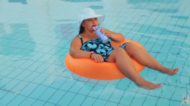 Güneş şapkalı neşeli kadın ve yüzme havuzunda mayo yavaşça yüzer ve dinlenir.