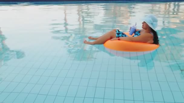 Brunette femme dans un chapeau et un maillot de bain dans la piscine dans un cercle de natation nage lentement — Video