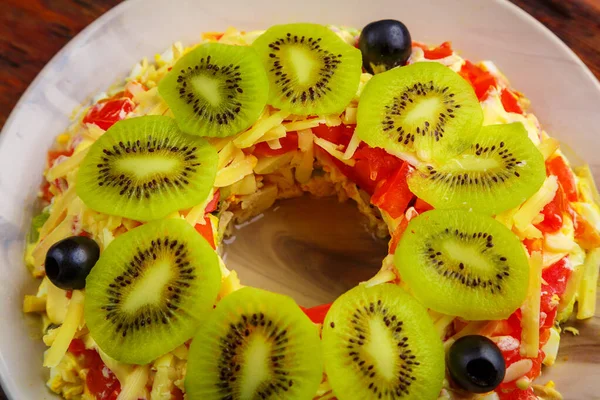 Puff salad with chicken breast and tomatoes, decorated with kiwi top view. — Stock Photo, Image