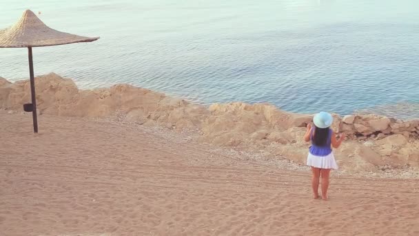 Ruskeaverikkö nainen sinisessä hatussa tanssii meren rannalla — kuvapankkivideo